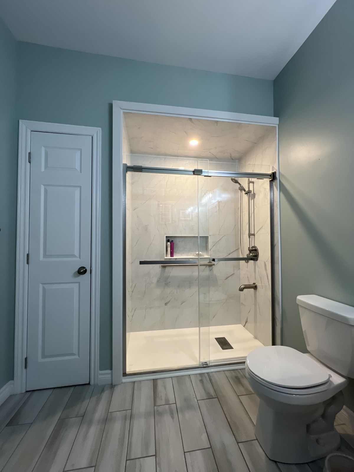 Same bathroom after a tub-to-shower conversion: low-profile shower base, marble-look wall panels, sliding glass doors and recessed niche